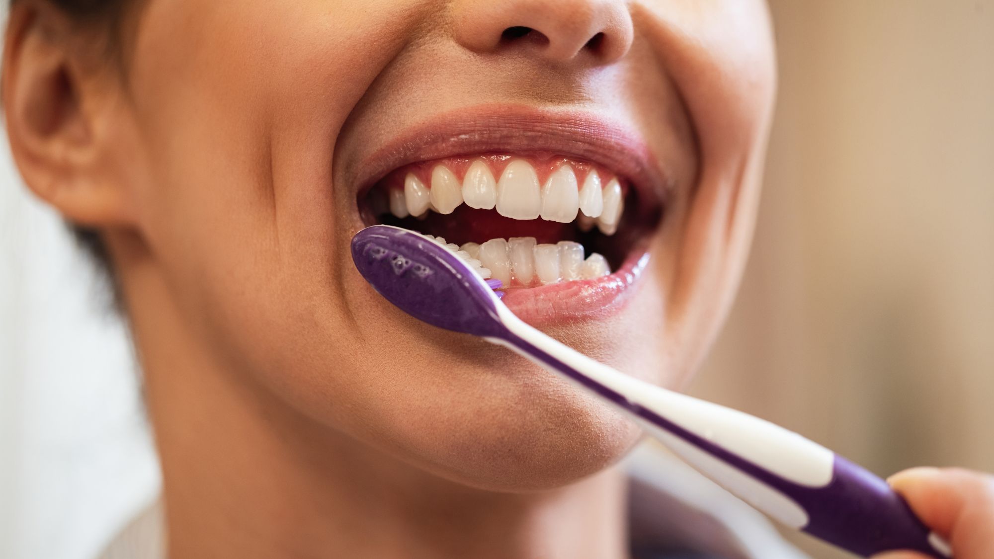 A woman smiling while brushing her teeth, showcasing natural teeth whitening